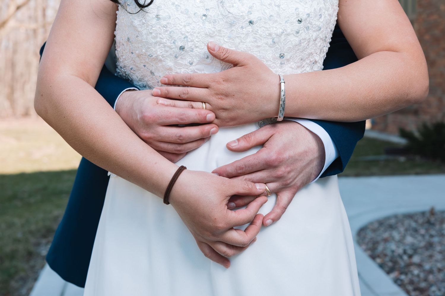 Close-up of bride and groom hands intertwined showing wedding rings and bracelets during wedding.