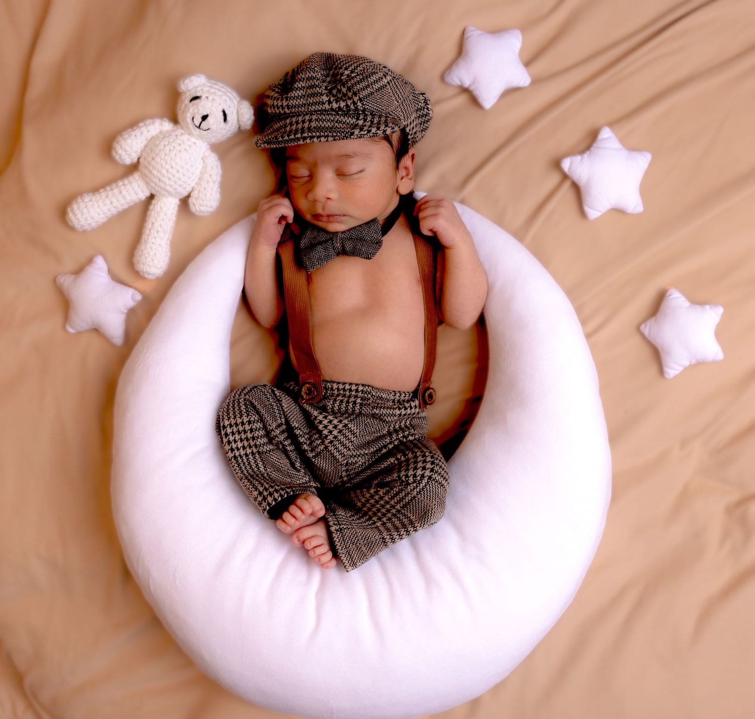 Newborn baby in vintage newsboy outfit sleeping on white moon pillow with star props.
