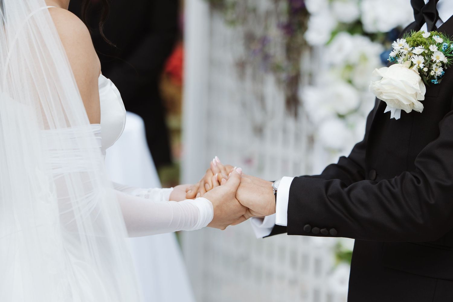 Close-up of bride and groom holding hands during outdoor wedding ceremony.