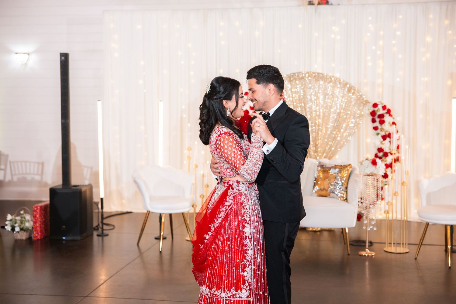 Indian bride in stunning red lehenga and groom in black tuxedo share romantic first dance at wedding.