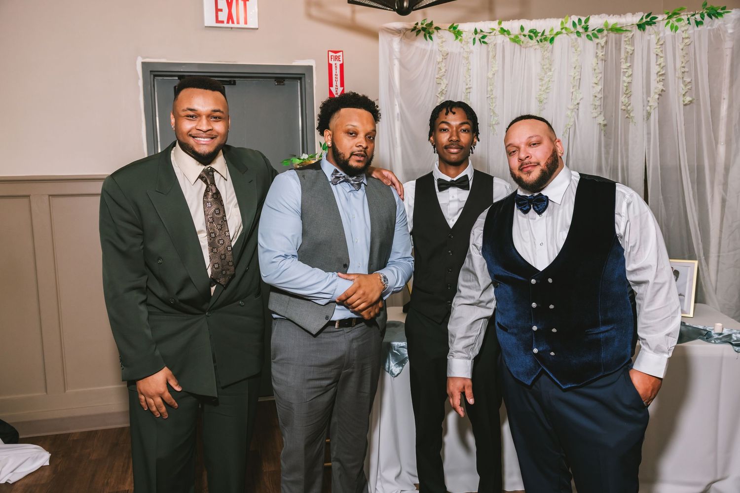 Four well-dressed men posing together at a wedding reception venue.