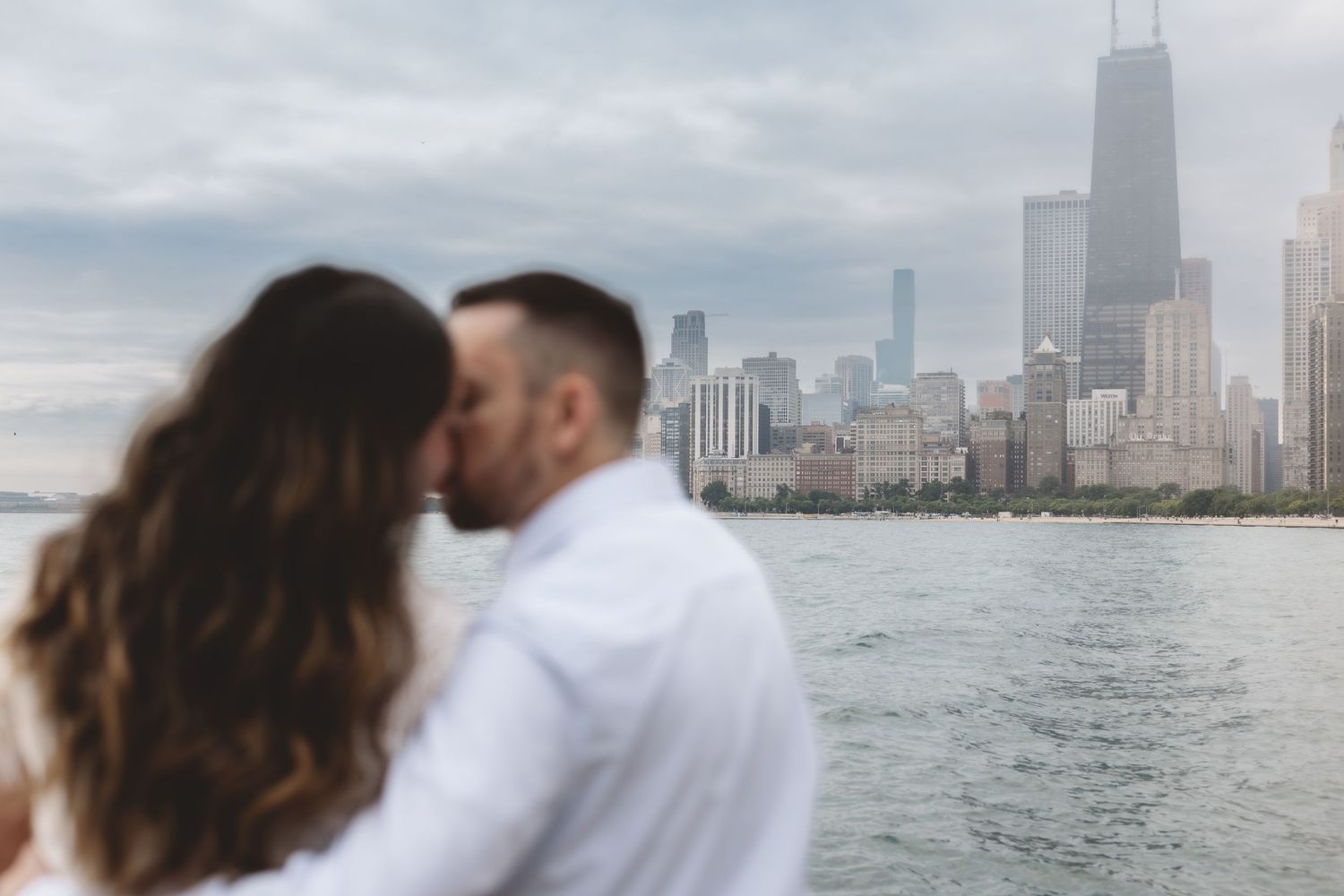 Couple sharing a romantic kiss with Chicago skyline in soft focus background.