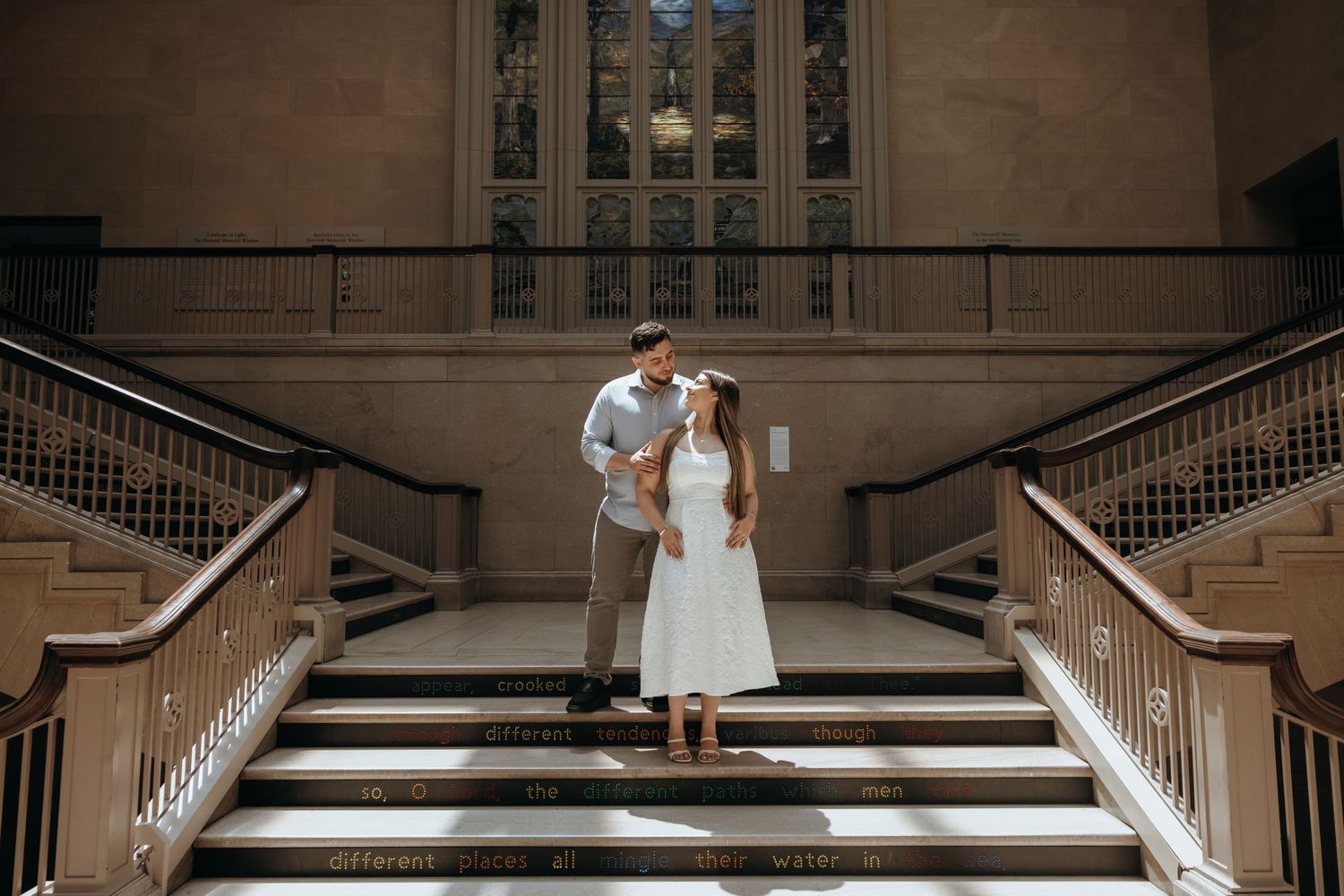 Couple shares romantic moment on ornate staircase of a historic museum during engagement photos.