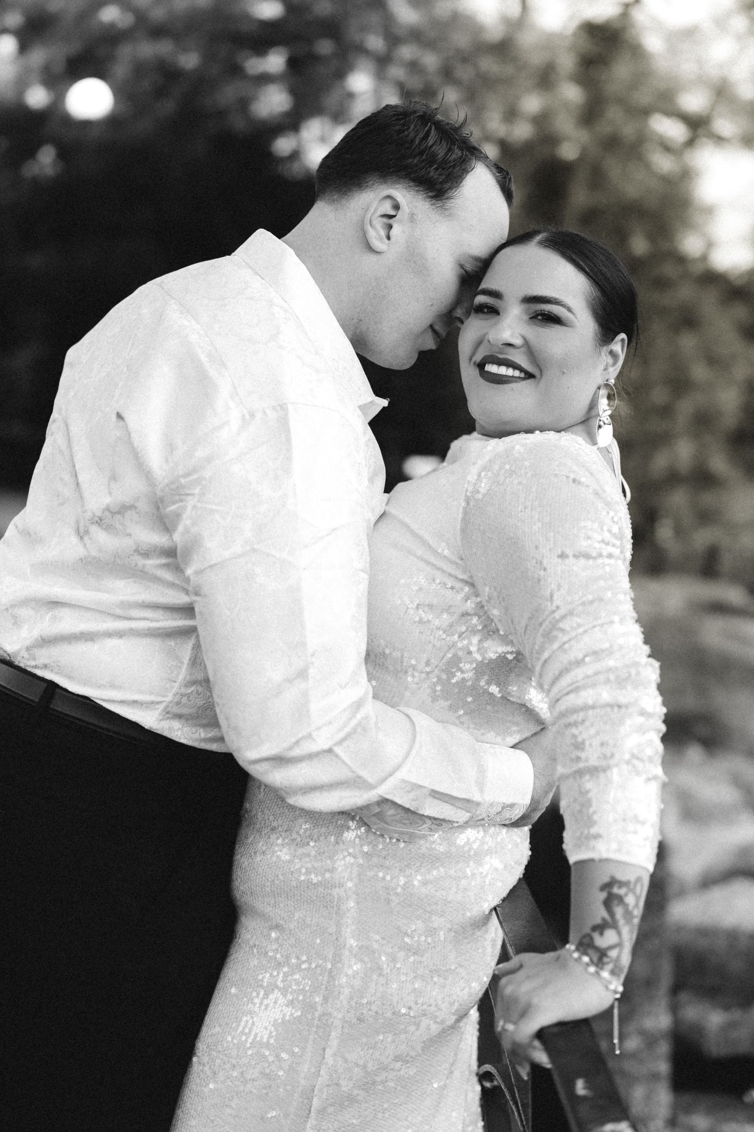 Black and white photo of smiling bride and groom embracing outdoors at their wedding.