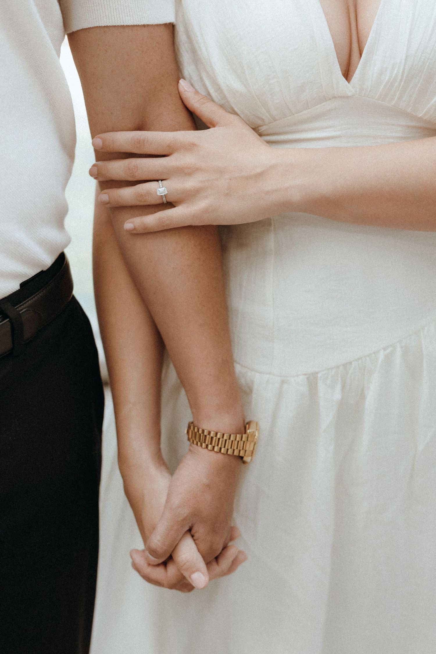 Close-up of engaged couple holding hands, woman wearing diamond ring and man wearing gold watch.