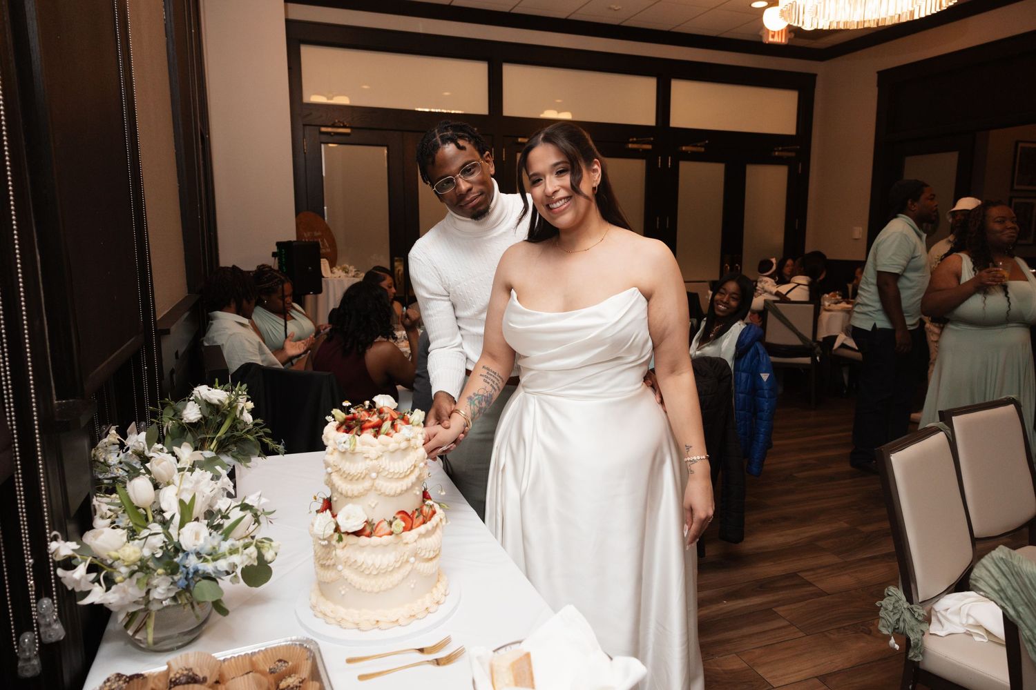 Newlyweds cutting white wedding cake together at elegant reception venue.