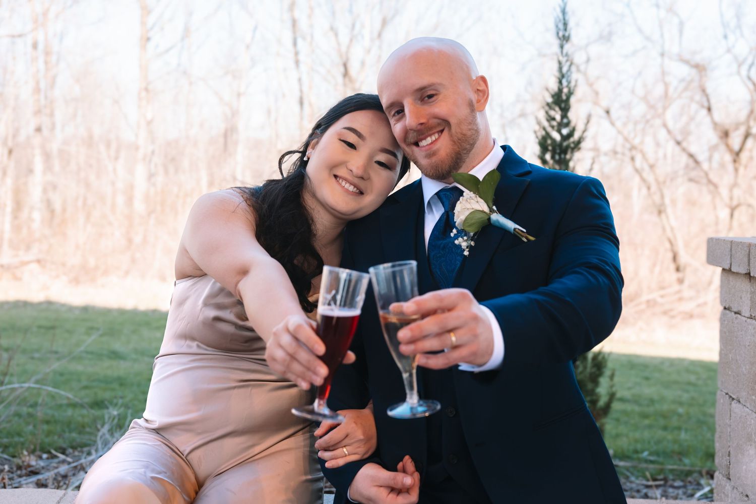 Happy couple clinking champagne glasses together during outdoor wedding celebration.