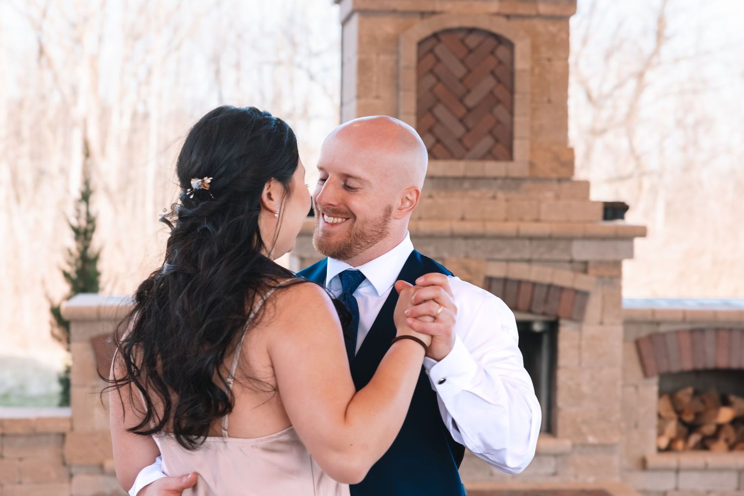 A smiling groom dances with his bride near a stone fireplace at an outdoor wedding reception.