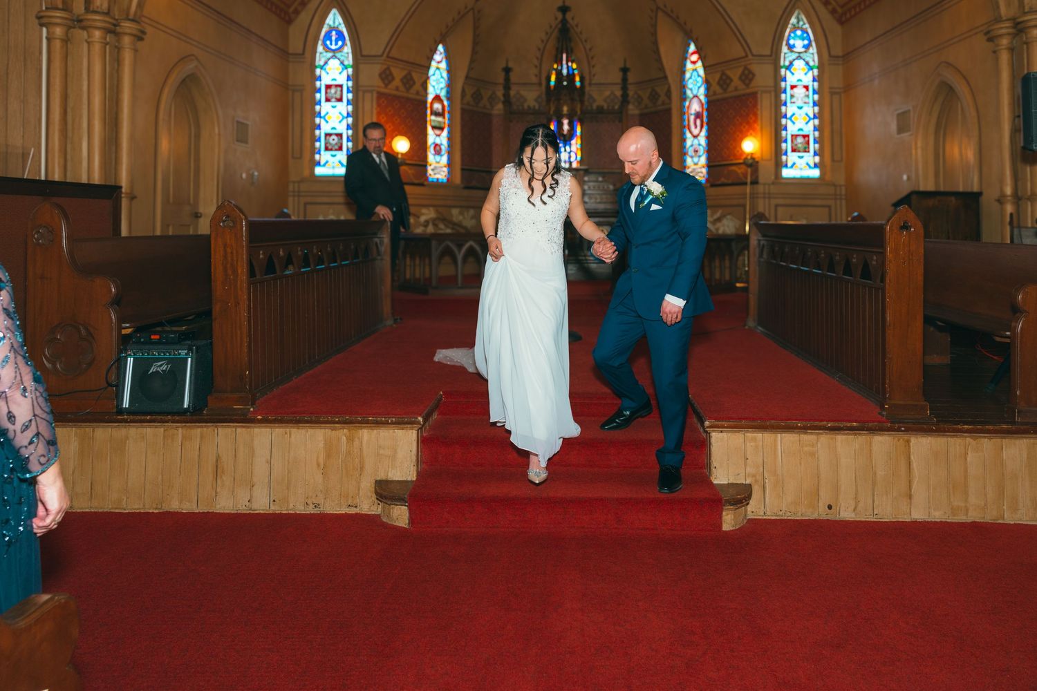 Bride and groom descend the church altar steps together in a beautiful historic church with red carpet aisle.