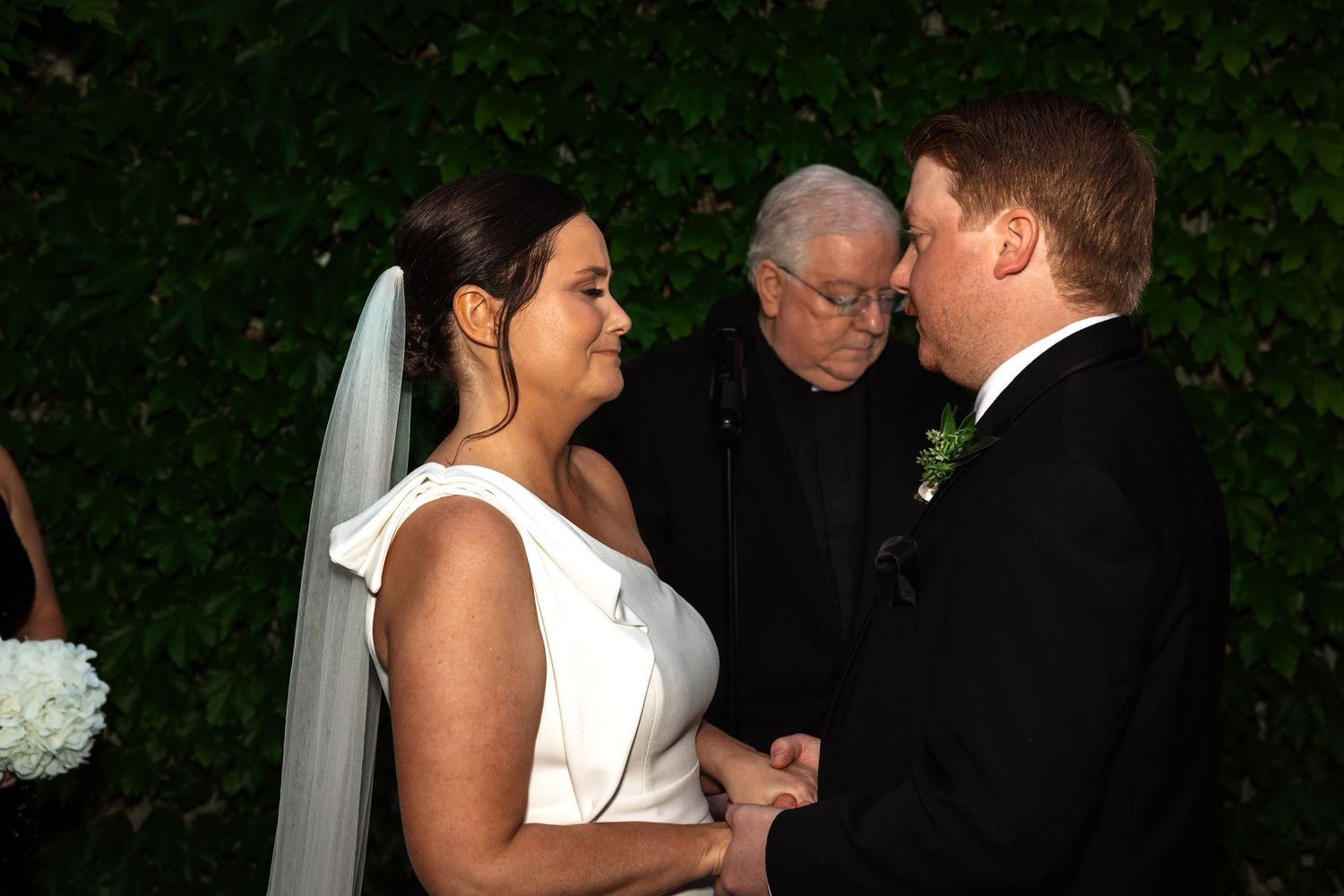 Bride and groom hold hands at altar with officiant during outdoor wedding ceremony.