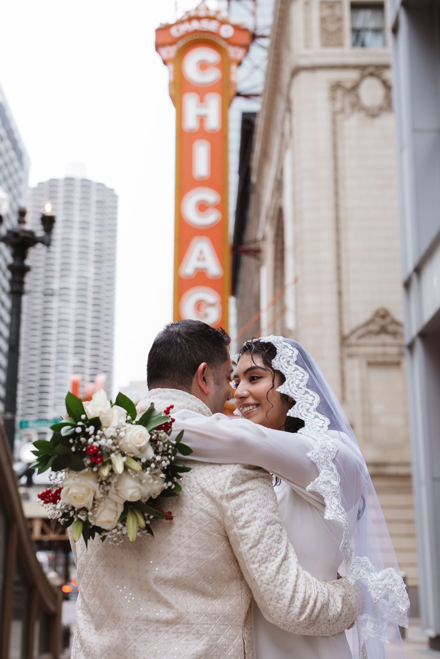 Smiling bride holds groom close with Chicago Theatre sign glowing orange in background.