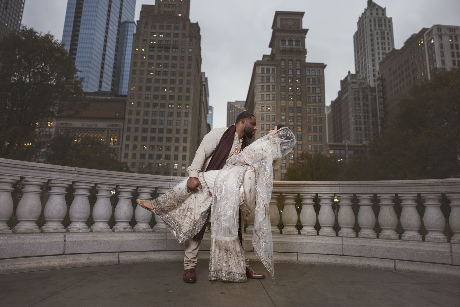 Couple in traditional South Asian wedding attire dancing on a terrace with NYC skyline backdrop.