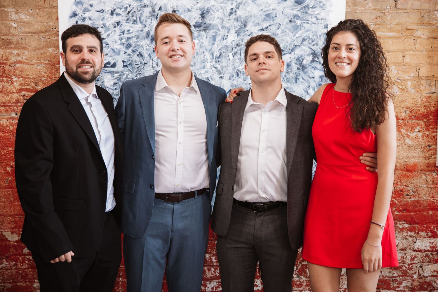 Four young professionals posing together at an art gallery event with brick wall background.