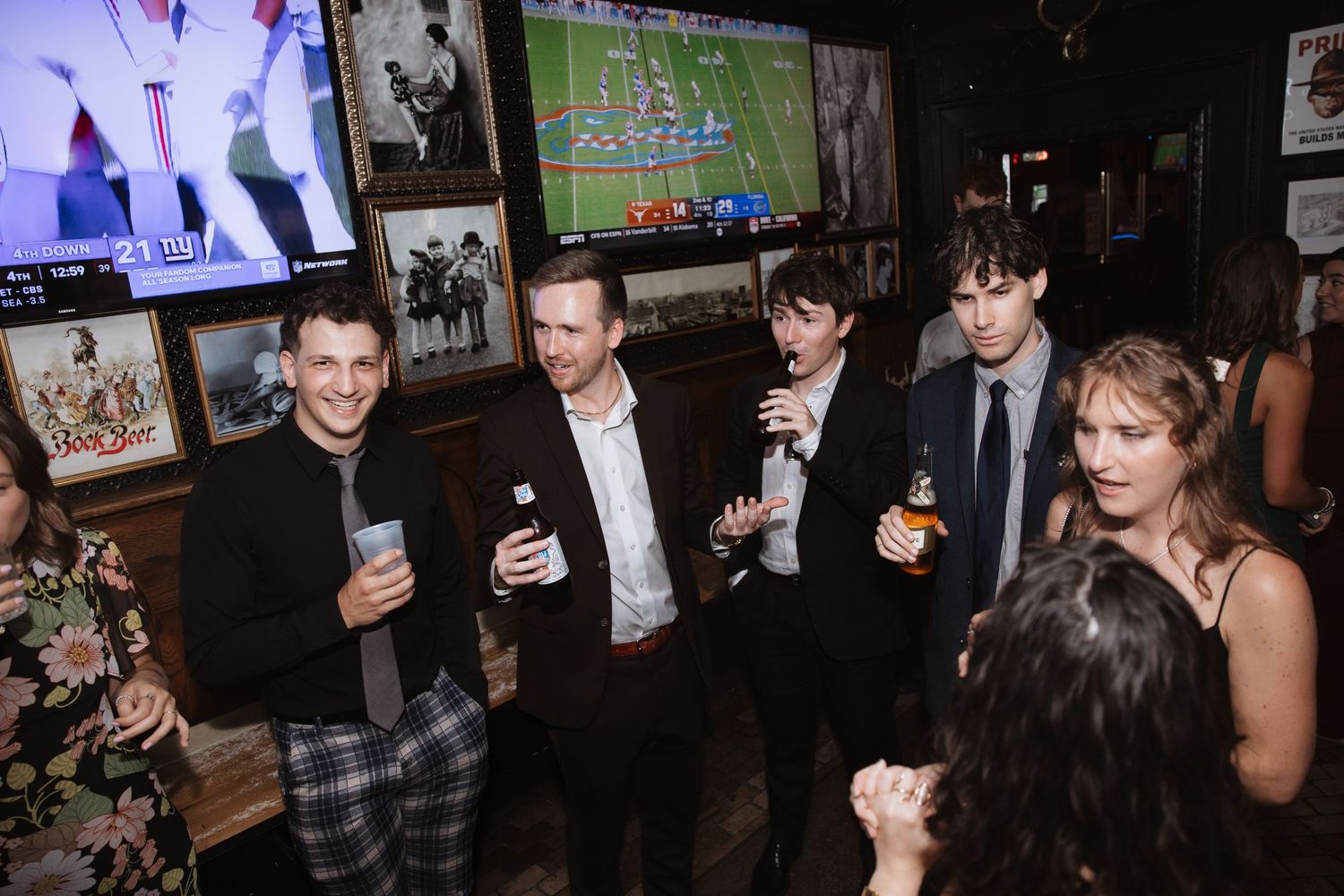 Group of young men in formal attire socializing at wedding reception watching sports TV.