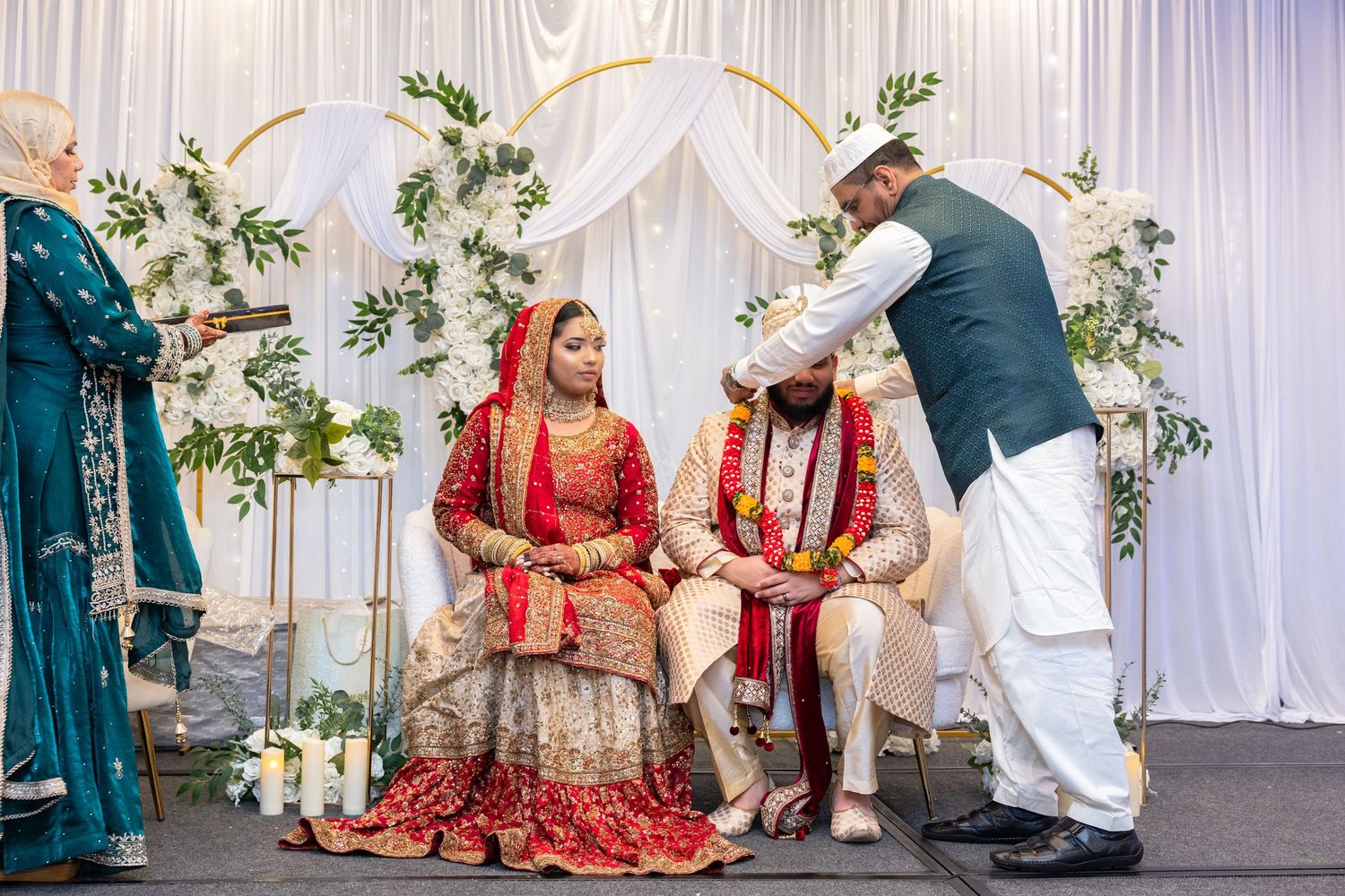 Bride and groom in traditional red and gold attire seated during South Asian wedding ritual.