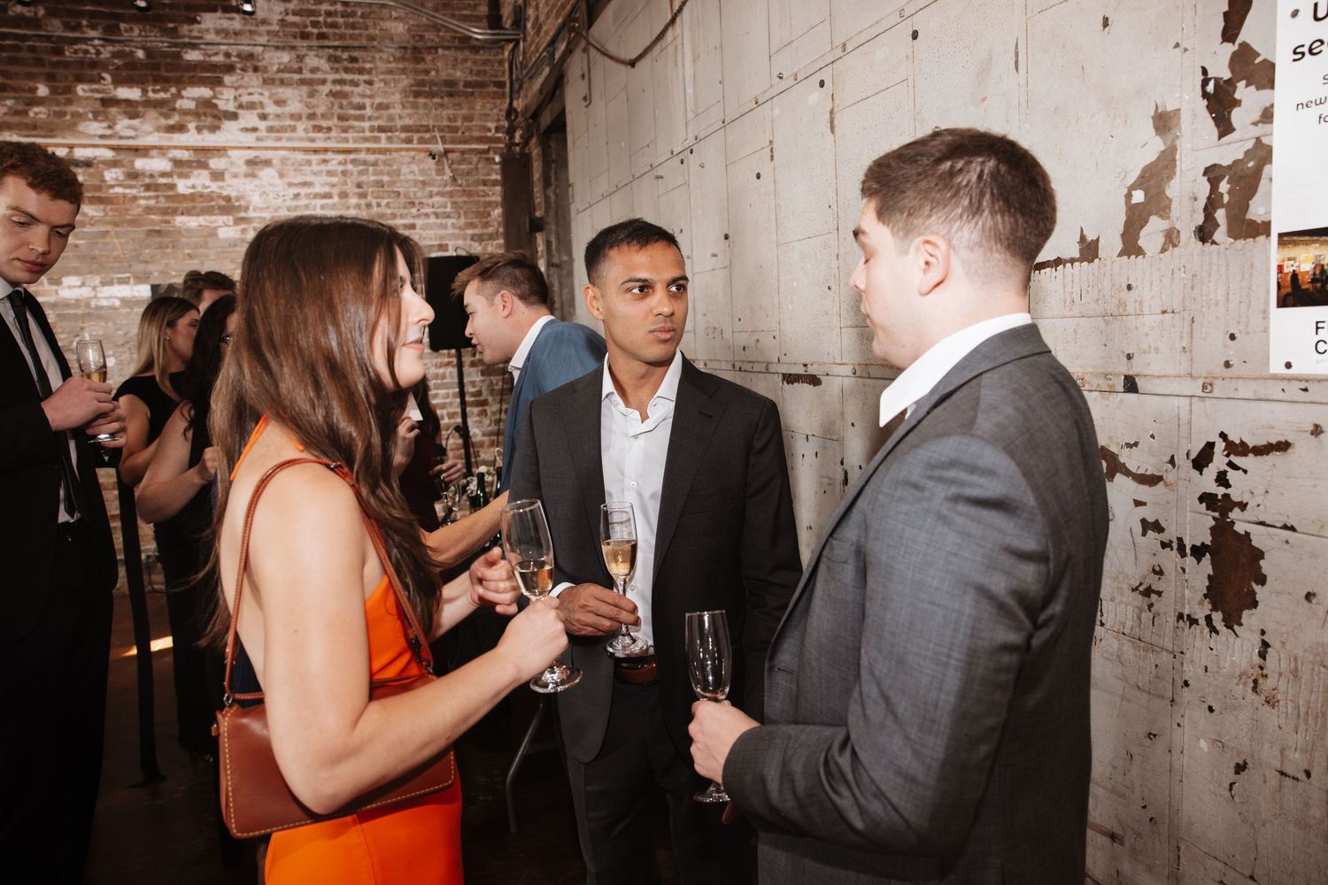 Three guests networking at an elegant event, holding champagne glasses in an industrial venue.
