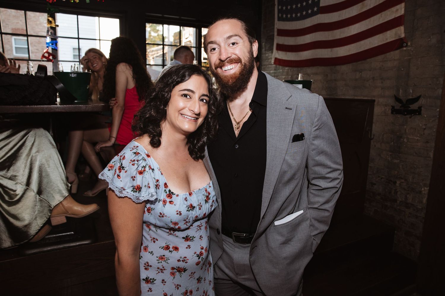 Smiling couple posing together at a casual bar event with brick walls.