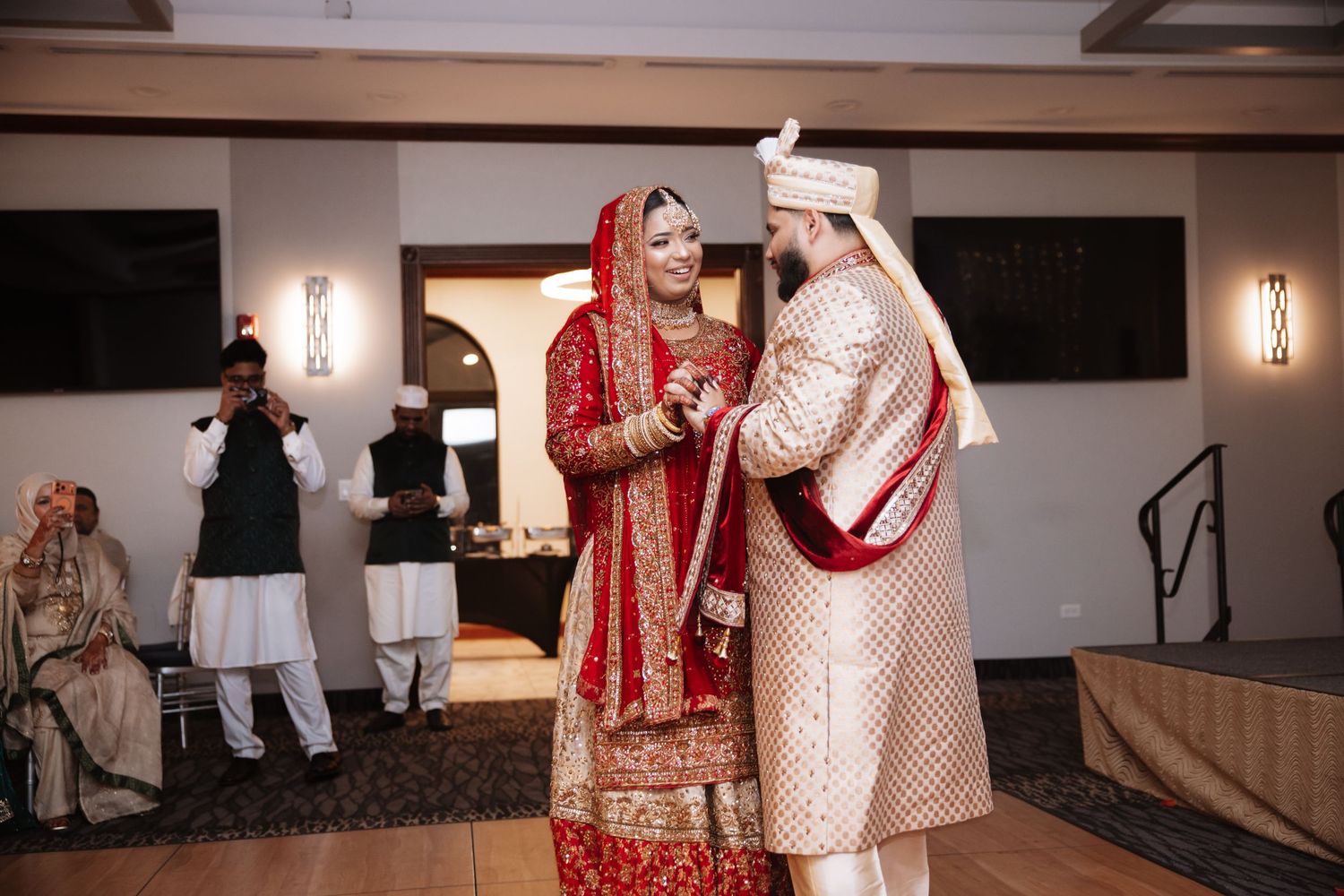 Bride and groom in traditional South Asian wedding attire sharing a joyful first dance.
