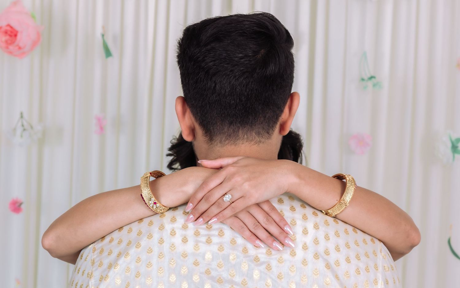 Couple embracing tenderly from behind showing diamond engagement ring and gold bangles at Indian wedding.