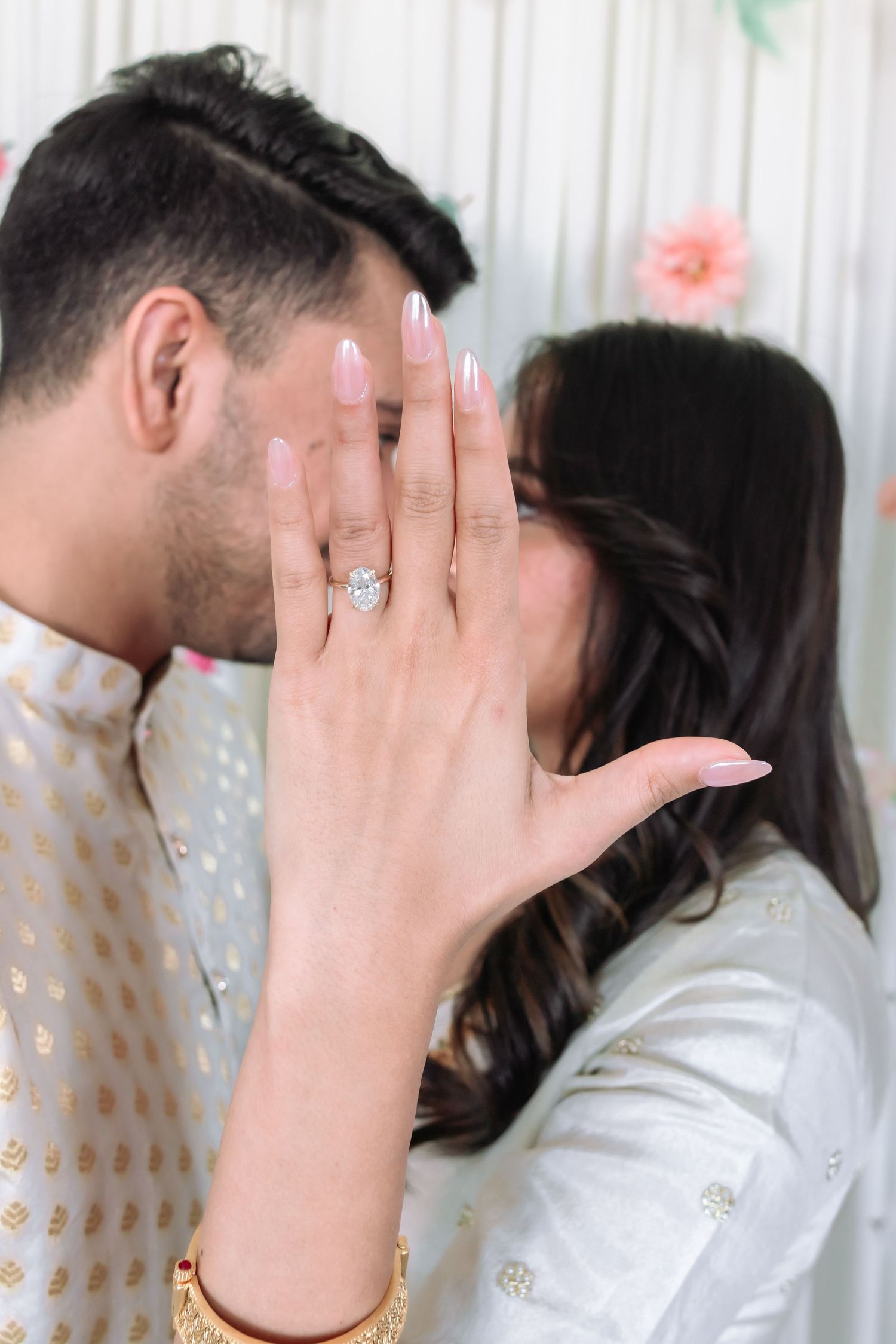 Indian couple kissing as bride displays diamond engagement ring to camera during wedding celebration.