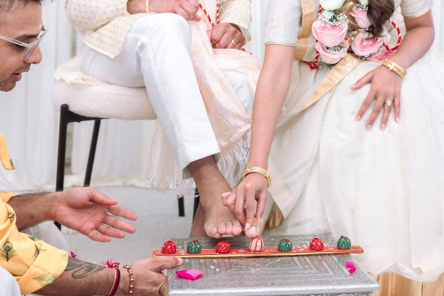 Close-up of a traditional Indian wedding foot ceremony with flower garlands and red toe rings.