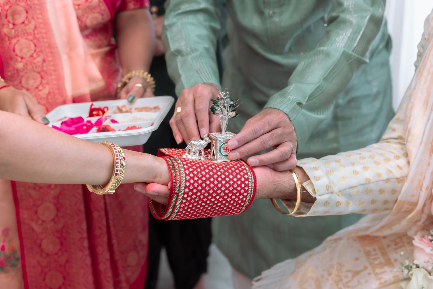 Close-up of Indian wedding bangles ceremony with red and gold chura bangles being placed on bride's wrist.