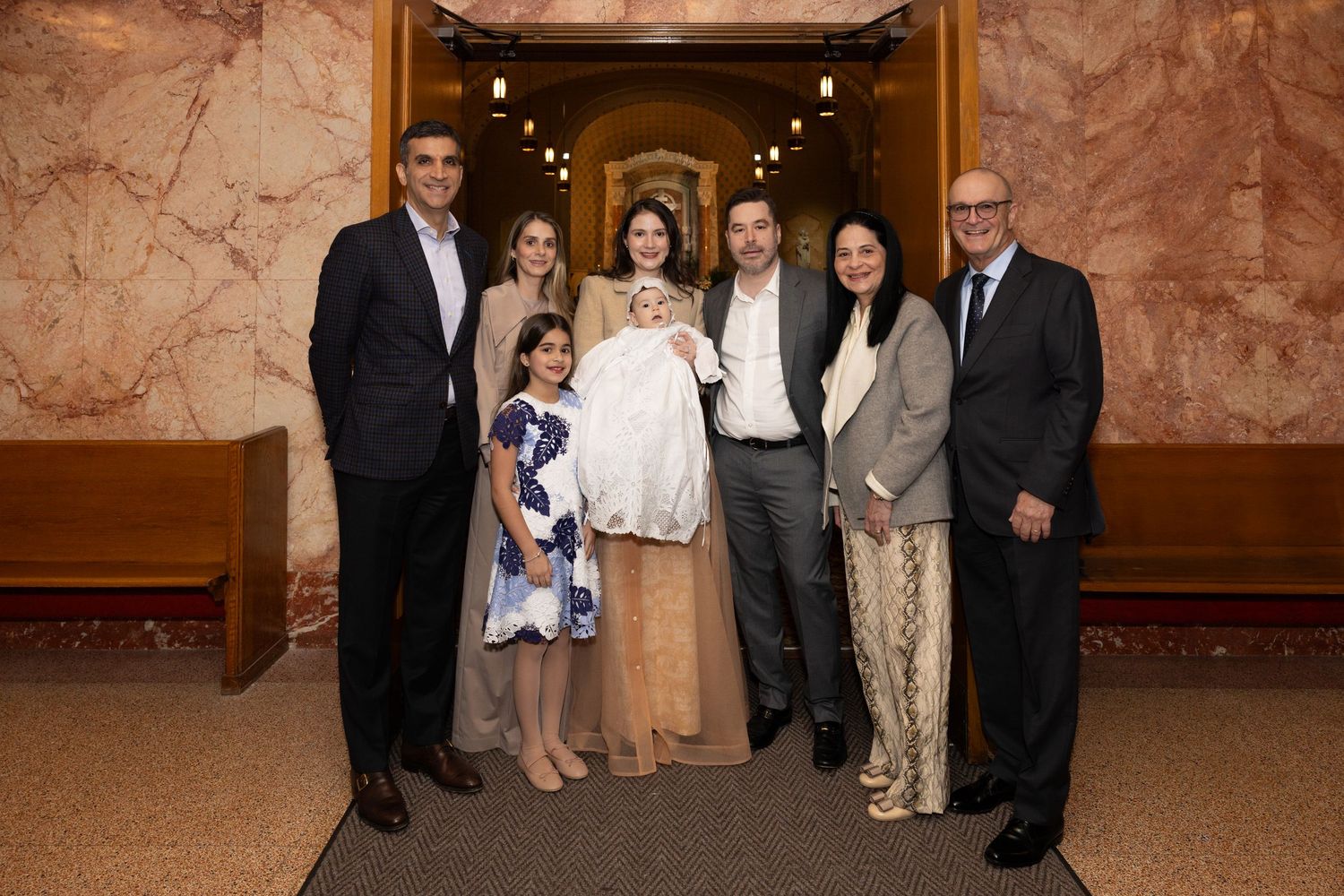 Family group of seven adults and a child pose together in a church lobby during a baptism celebration.