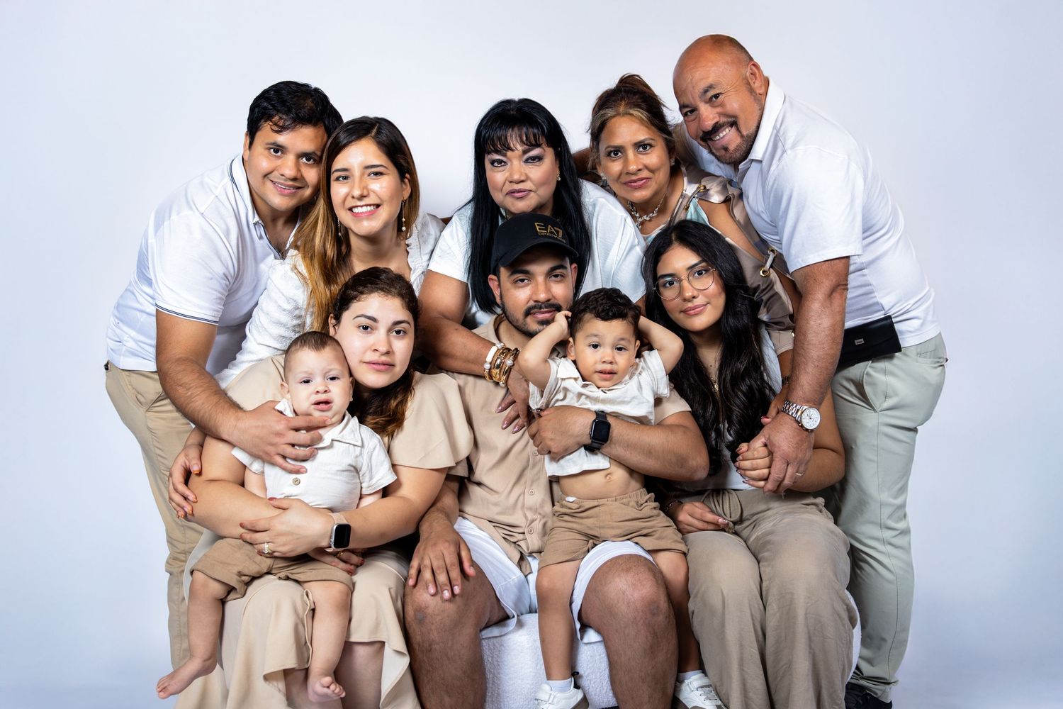 Large Hispanic family group portrait with babies in coordinating white and beige outfits.