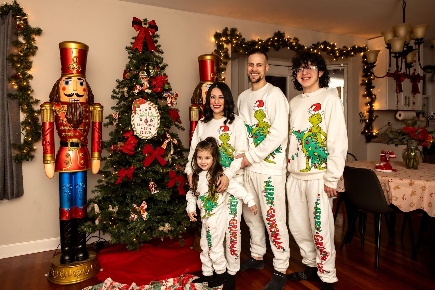Family of four in Grinch Christmas pajamas standing by holiday tree.