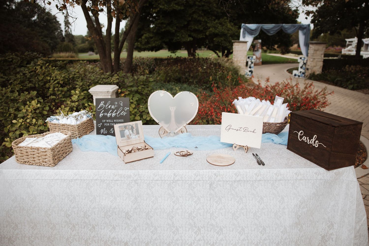 Elegant outdoor wedding welcome table with guest book, cards box, and heart decorations.