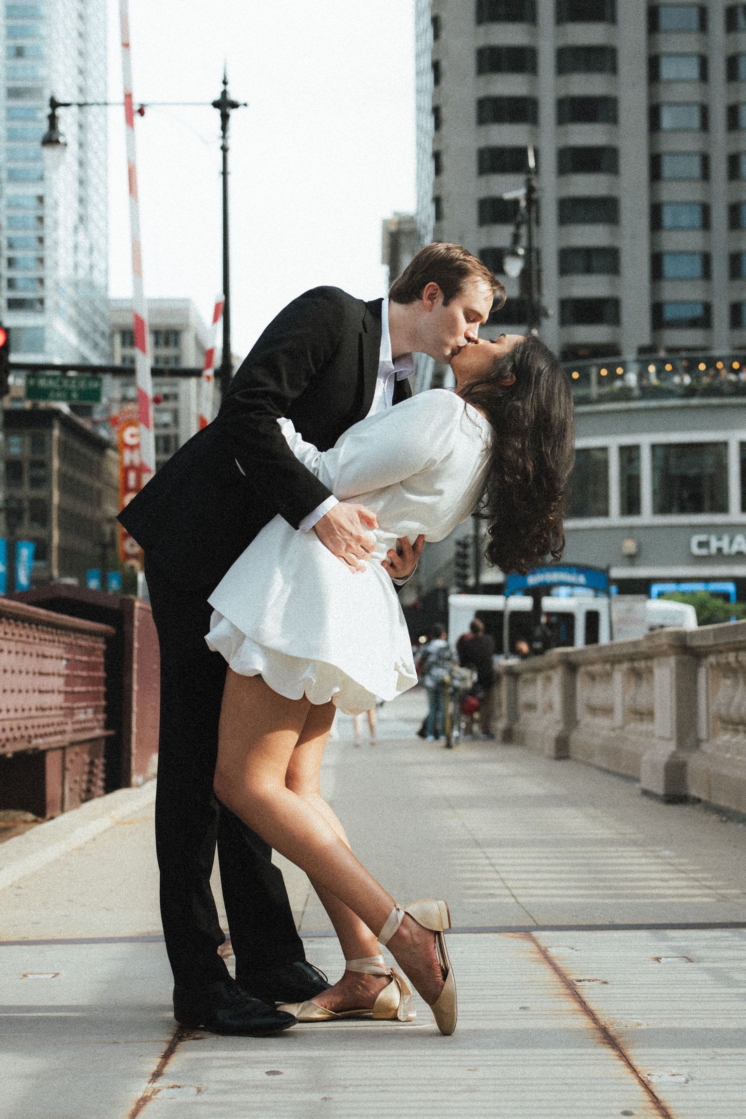 Couple sharing a romantic dip kiss on a Chicago bridge with city buildings in the background.