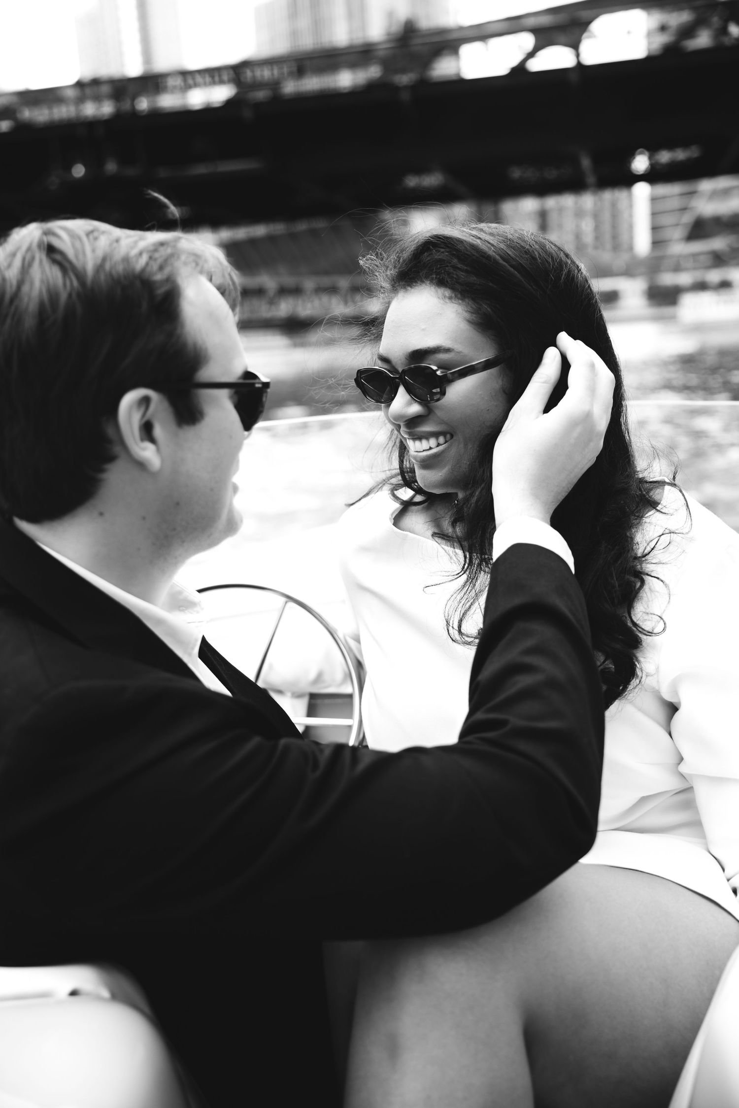 Black and white photo of a smiling couple in sunglasses sharing a romantic moment on a boat.