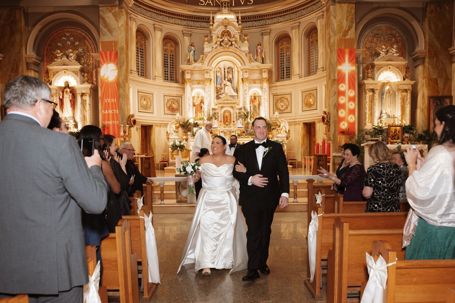 Bride and groom walk down the aisle of an ornate Catholic church after their wedding ceremony.