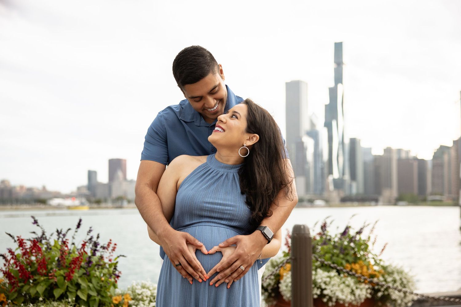 Loving pregnant couple forming heart with hands over baby bump against Chicago city skyline backdrop.