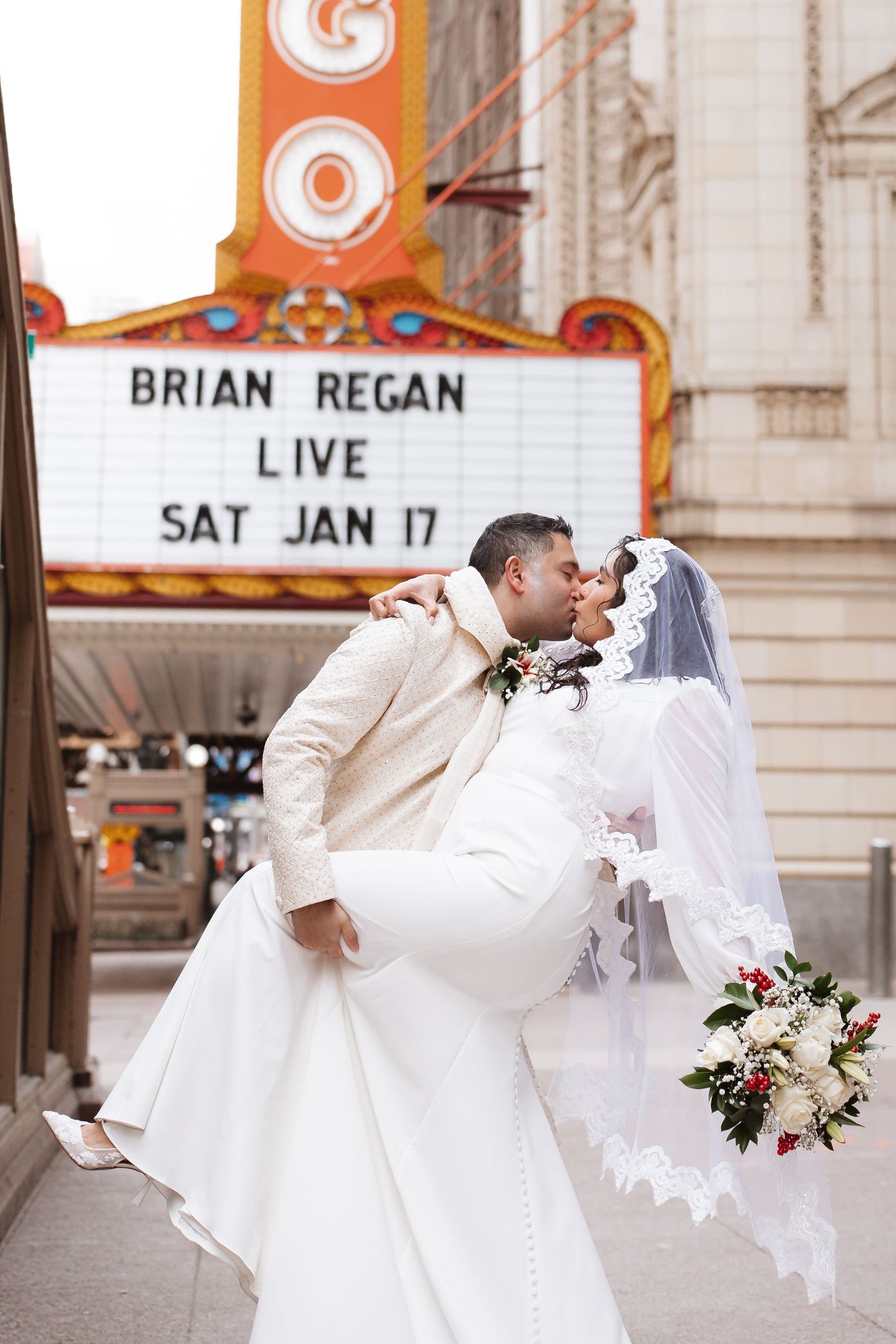 Groom lifts bride in white gown for a kiss outside the iconic Chicago Theatre marquee.