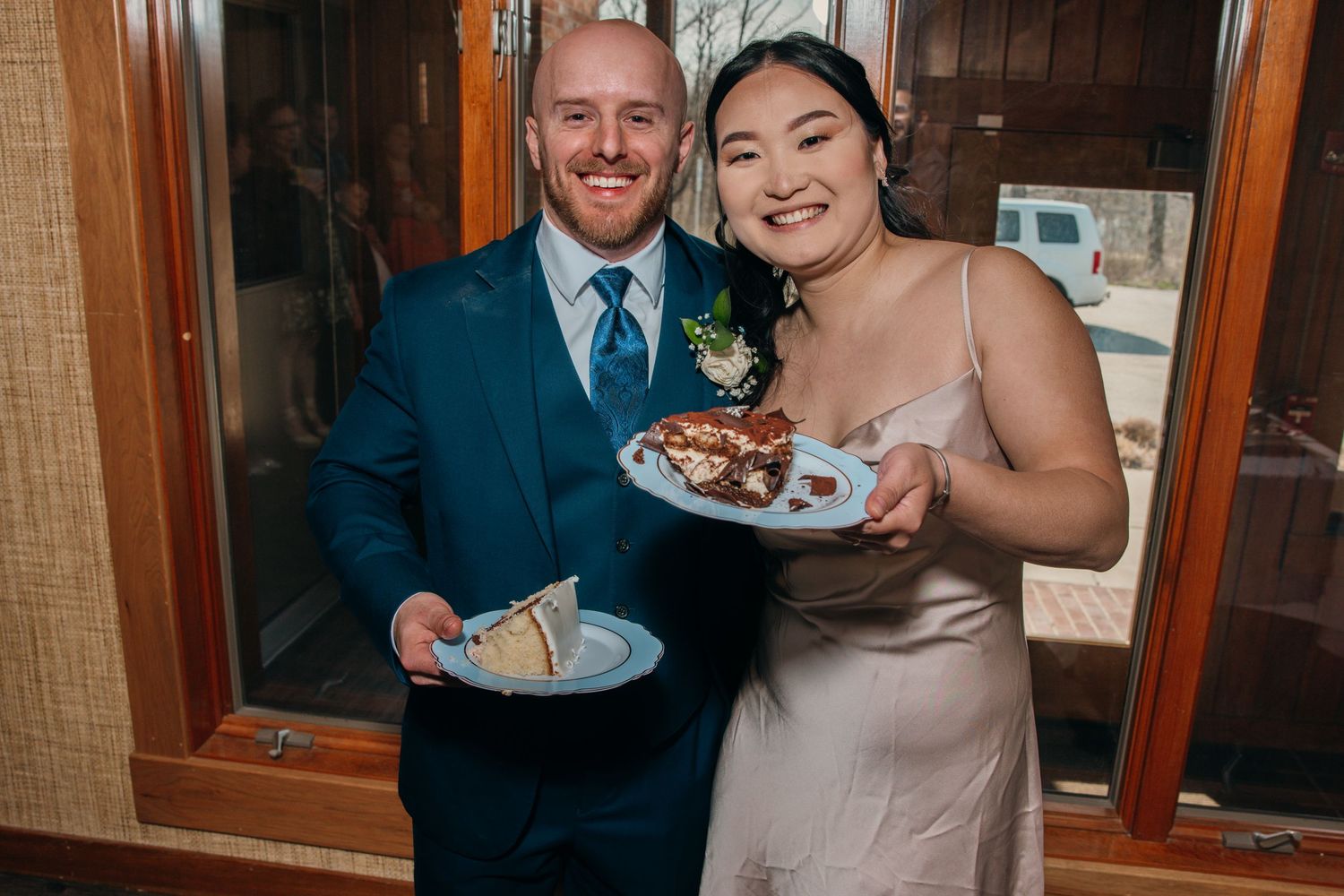 Happy newlyweds smiling and holding plates of food at their wedding reception dinner celebration.