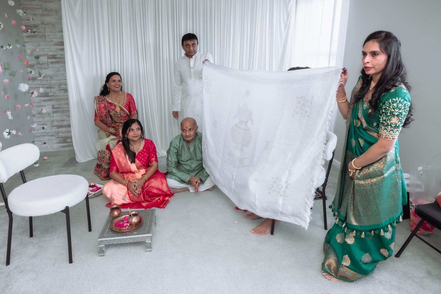 Indian family displays embroidered white wedding cloth during traditional Hindu wedding ceremony indoors.