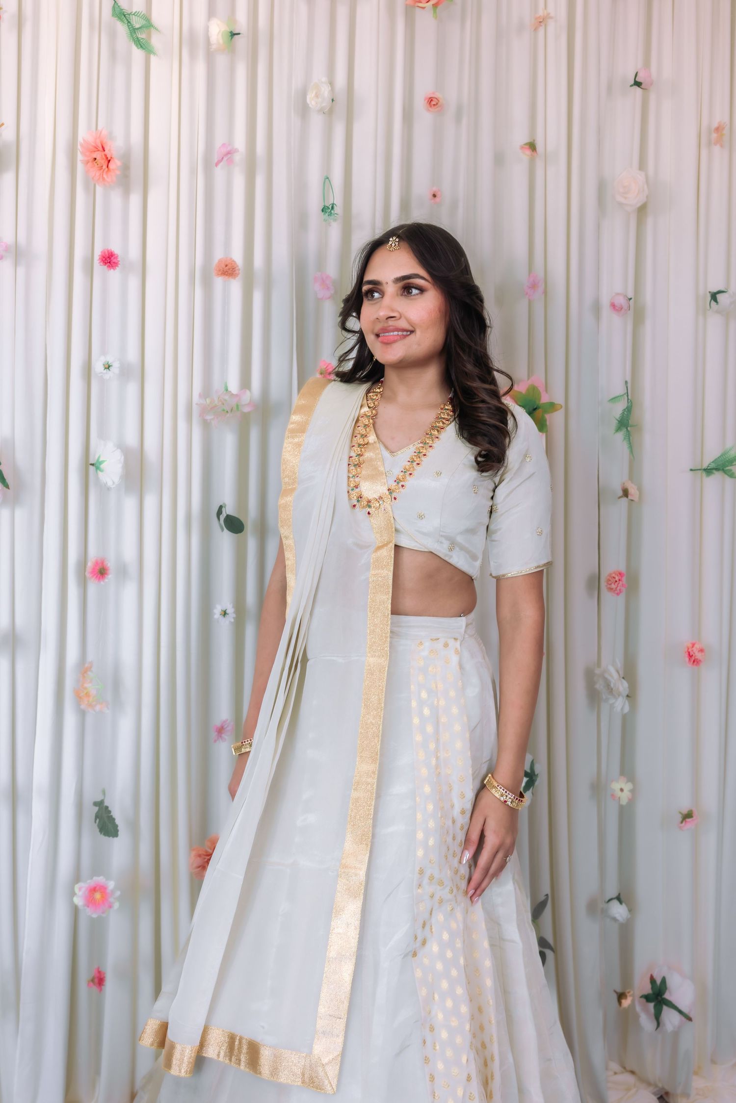 Beautiful Indian bride in white gold lehenga smiles wearing traditional gold jewelry at wedding event.