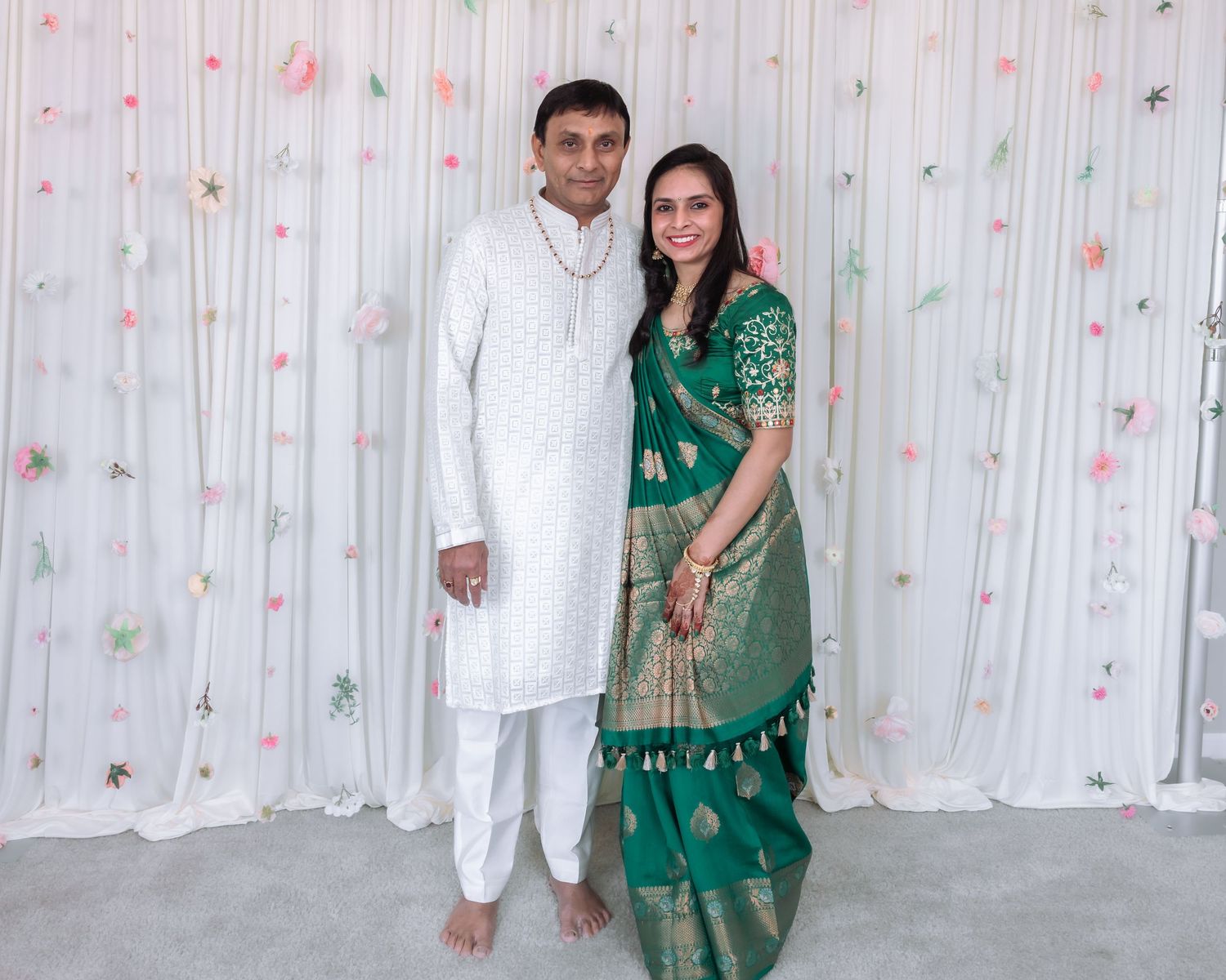 Couple in traditional Indian attire, man in white kurta and woman in green silk saree, posing at a celebration.