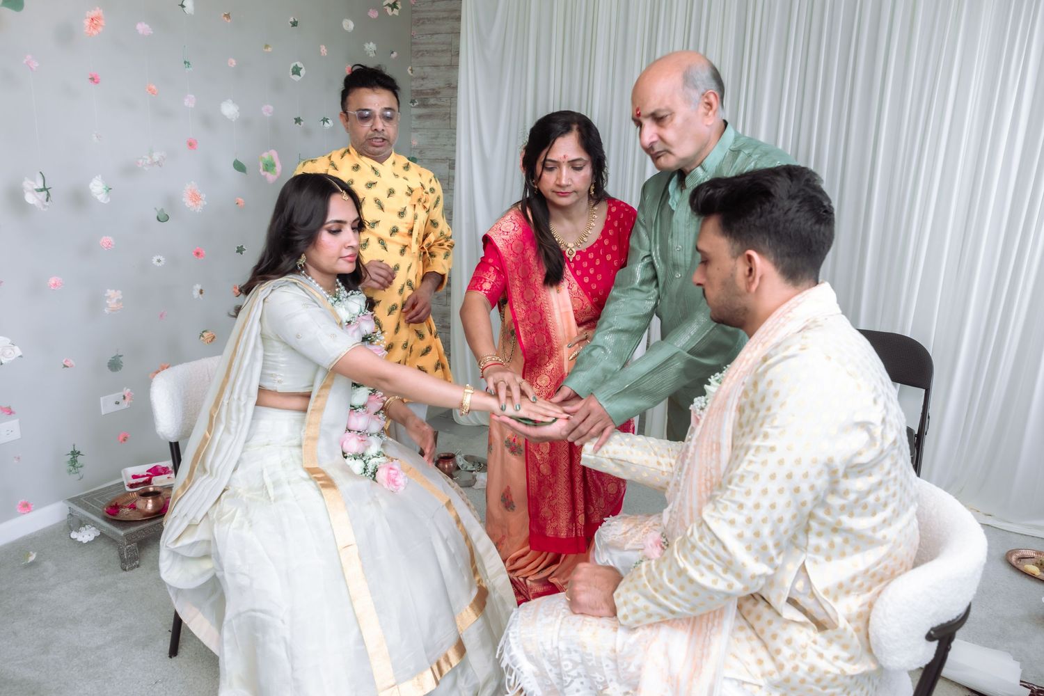 Indian wedding ceremony with bride in white lehenga and groom in sherwani performing traditional hand ritual.