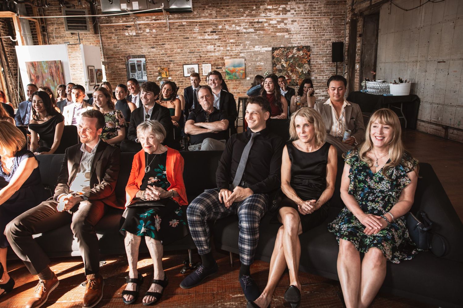 Wedding guests seated and smiling during ceremony in rustic brick loft venue.