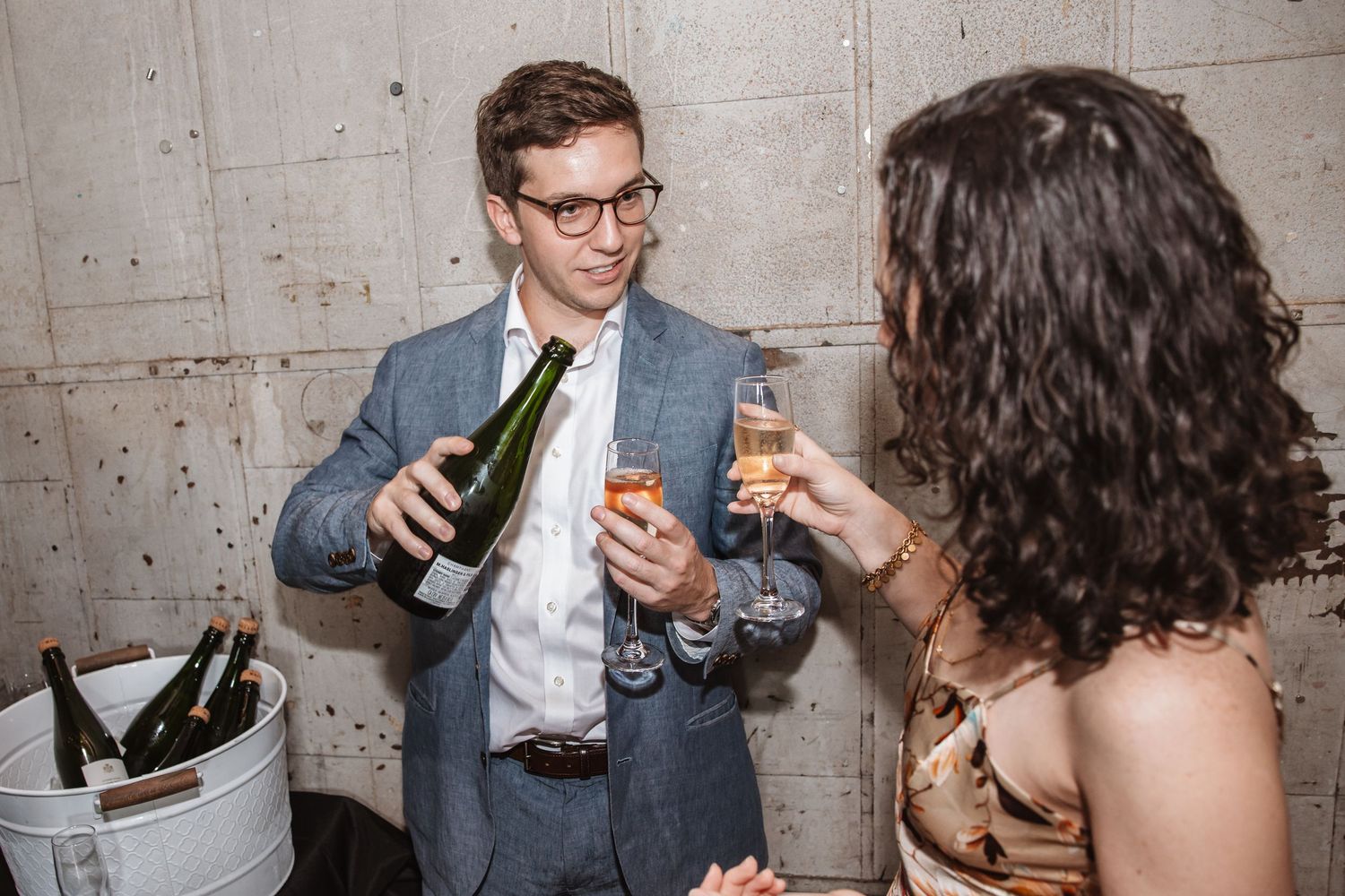 Young man in grey suit pouring champagne for a woman at an elegant reception event.