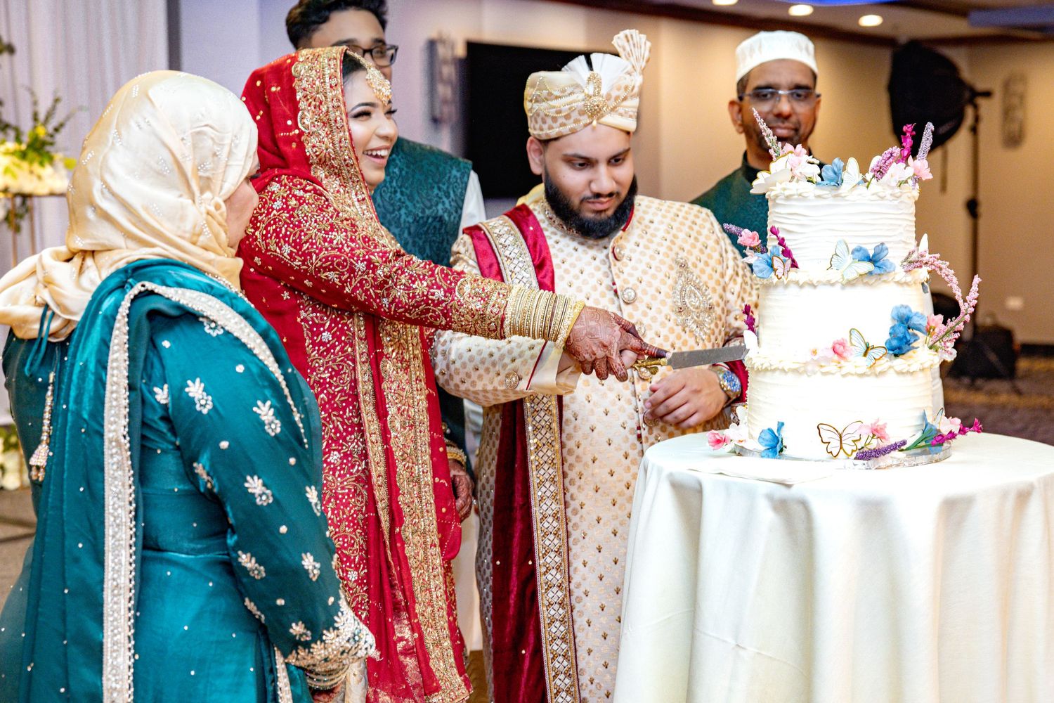 Couple in traditional South Asian wedding attire cutting a decorated cake.