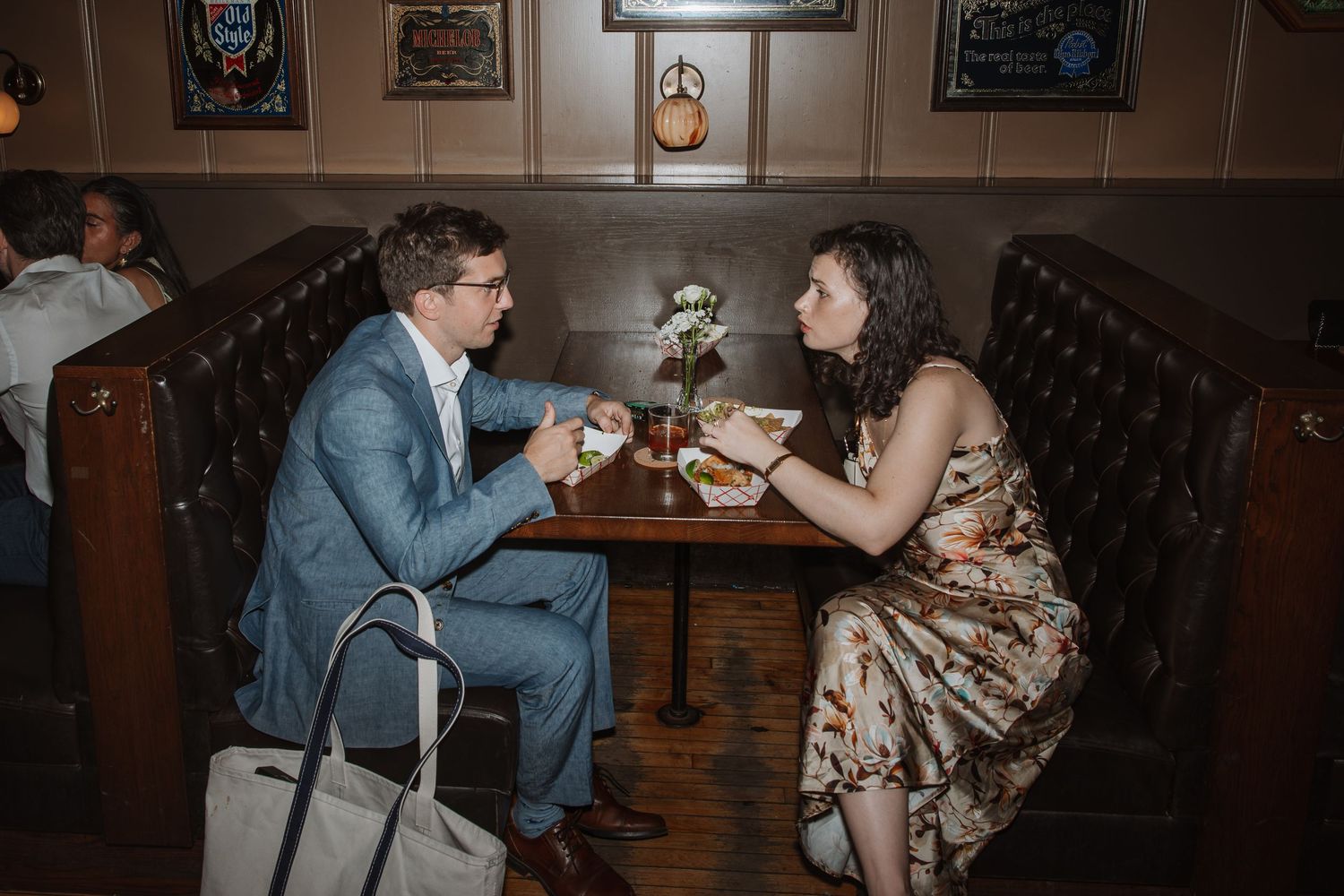 Couple in formal attire sharing an intimate conversation over drinks at a restaurant booth.