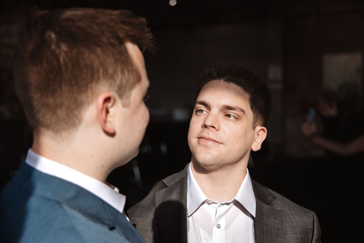 Two men in suits engage in conversation at a formal event in a dimly lit venue.