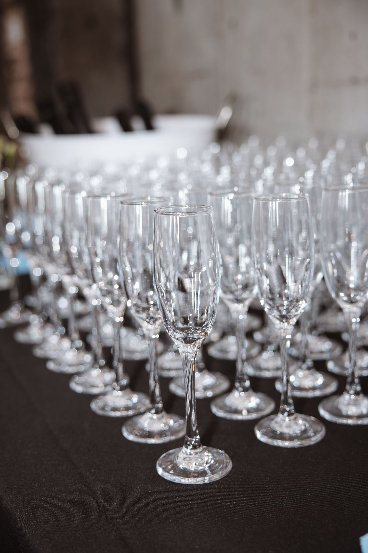 Rows of empty crystal champagne flutes arranged on a black tablecloth for an event.