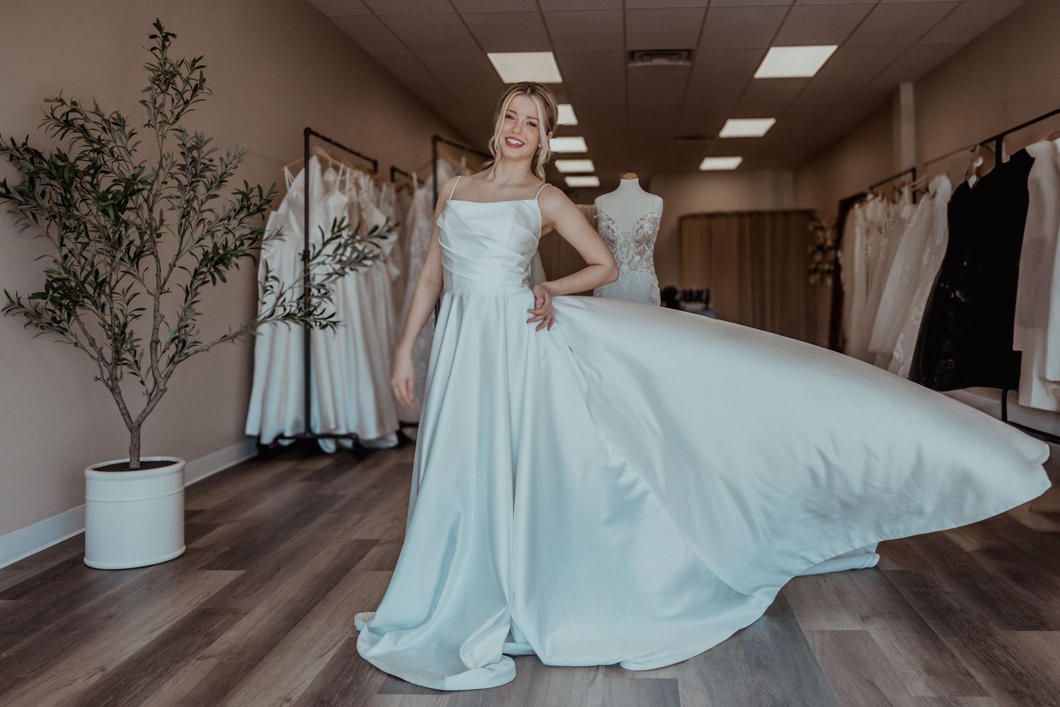 Blonde bride joyfully twirling in flowing white satin ball gown wedding dress in bridal shop.