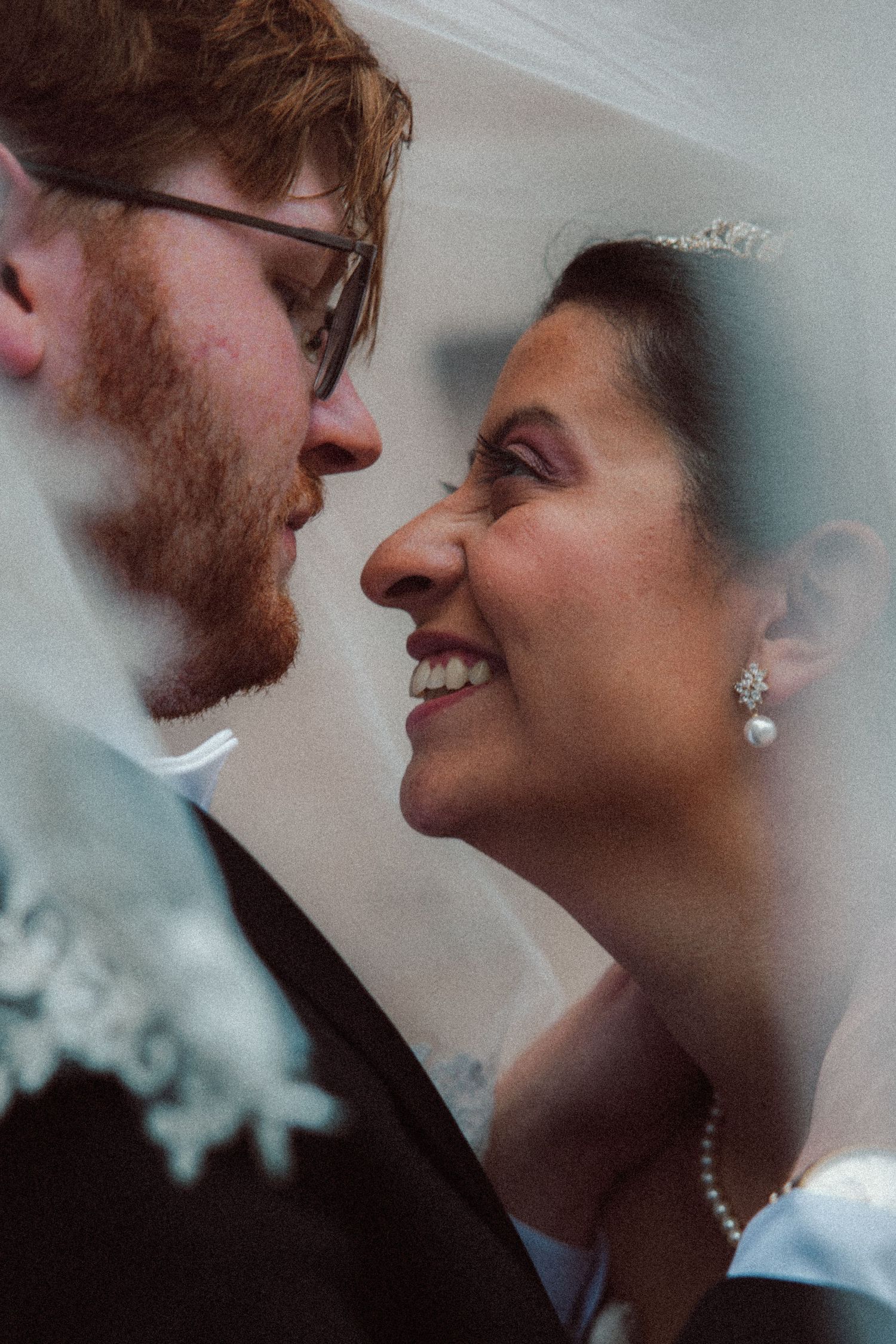 Bride and groom sharing an intimate moment under a veil, bride smiling joyfully.
