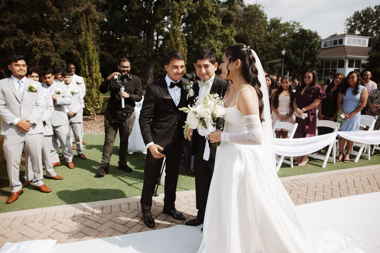 Groom reaches for bride's hand as she arrives at the altar during an outdoor wedding ceremony.