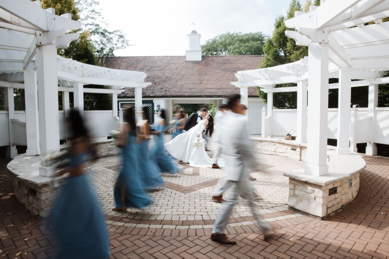 Wedding party walking through elegant white pergola courtyard with motion blur effect.